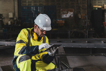 Mechanical Engineer in Hard Hat Wearing Safety Jacket Uses tablet working in the Manufacturing Factory