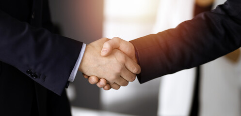 Obraz premium Unknown businesspeople are shaking their hands after signing a contract, while standing together in a sunny modern office, close-up. Business communication, handshake, and marketing concept