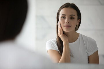 Beauty needs care. Pretty young lady doing daily morning skincare procedures, cleansing face skin...