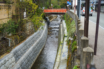Fototapeta premium 道路の脇を流れる小川と小さな赤い橋