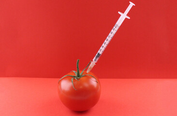 Syringe in red tomato on red background
