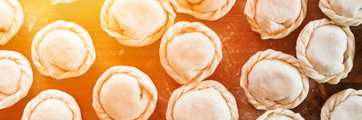 pile of small homemade uncooked dumplings with meat on kitchen table. national traditional Russian cuisine. do it yourself. top view, flat lay. banner. flare