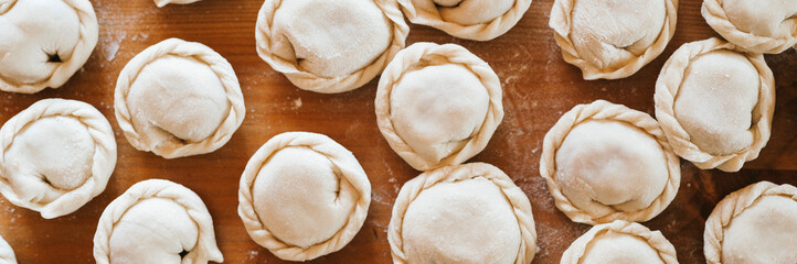 pile of small homemade uncooked dumplings with meat on kitchen table. national traditional Russian cuisine. do it yourself. top view, flat lay. banner