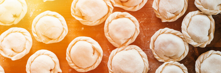pile of small homemade uncooked dumplings with meat on kitchen table. national traditional Russian cuisine. do it yourself. top view, flat lay. banner. flare