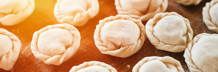 pile of small homemade uncooked dumplings with meat on kitchen table. national traditional Russian cuisine. do it yourself. top view, flat lay. banner. flare