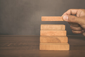 Close-up hand is placing wood block tower stacked in stair step with caution to prevent collapse or crash concepts of financial risk management and strategic planning.