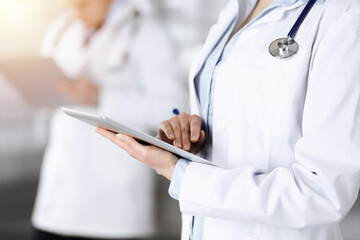 Unknown woman doctor is checking some data at computer tablet, close up. Young doctors at work in a sunny hospital. Modern medicine and healthcare concept