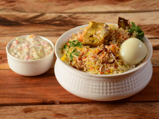 Traditional Hyderabadi Chicken dum Biryani made of Basmati rice cooked with masala spices, served with boiled egg and Onion raita, selective focus
