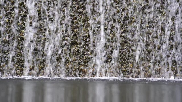 Water falling pouring into a poolside from stone wall, close up. Background with running water. Waterfall fountain stri and spray drops stone surface.