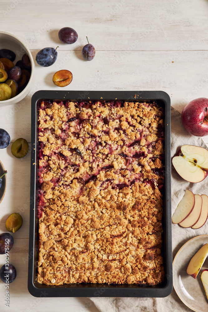 Sticker Top view of freshly baked plum and apple cake in a pan and fresh plums and apples on a white table