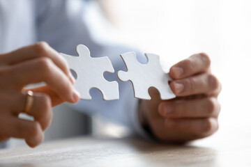 Close up young entrepreneur putting different parts of puzzles together, making business decision, finding creative logical problem solution or developing strategy brainstorming alone in office.