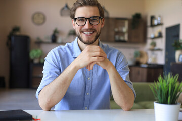 Confident happy businessman in eyeglasses sitting at home workplace and looking at camera.