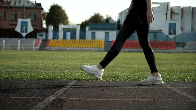 young caucasian woman preparing to run at stadium, side view in slow motion. fitness runner in sportswear starts running on stadium track. fit sportive female in starting position. healthy lifestyle