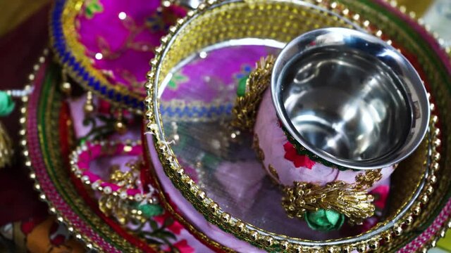 panning shot of a decorated thali for karva chauth with ribbon decorations, sieve, pot of water, lota, and danglers in preparation for the hindu festivals of diwali, vrat and more. Shows the decoratio