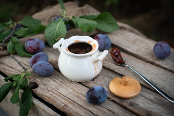 plum jam in a white ceramic pot on an aged wooden background, fresh plums near