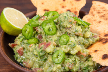 Homemade guacamole - traditional mexican appetizer of avacado, onion and tomato in a bowl with pieces of toasted tortilla on a rustic wooden table,  top view