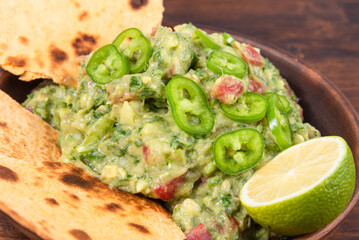 Homemade guacamole - a traditional Mexican appetizer of avacado, onion and tomato in a bowl with pieces of toasted tortilla on a rustic wooden table, close-up