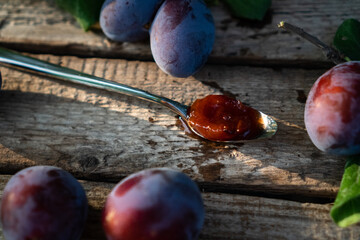 dessert steel spoon with plum jam on an aged wooden background, fresh plums near