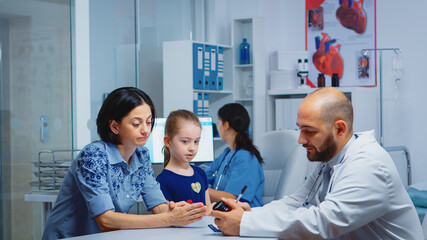 Doctor holding pills bottle and writing instructions while talking with parent in clinic. Physician, specialist in medicine providing health care services consultation diagnostic treatment in hospital