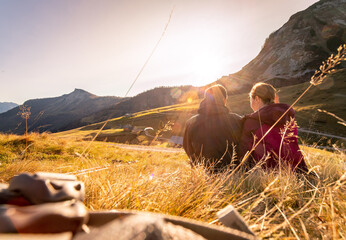 Loving couple is enjoying the sundown in the mountains, sitting on the ground. Warm colors, alps, Austria - obrazy, fototapety, plakaty