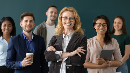 Aged leader of diverse team. Portrait of pleasant confident older lady businesswoman ceo trainer mentor coach standing in front of happy multiethnic workforce staff group smiling and looking at camera - obrazy, fototapety, plakaty
