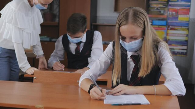 The teacher in the classroom explains a new topic to students. Masked children, post-quarantine life, new normality after lockdown, coronavirus covid-19. Back to school