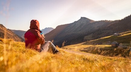 Fototapeta premium Hiking girl is enjoying the sundown in the mountains, sitting on the ground. Warm colors, alps, Austria