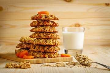 Delicious sweet oatmeal with dried apricots, nuts, a spoonful of oatmeal and a glass of milk in the background on a wooden table.