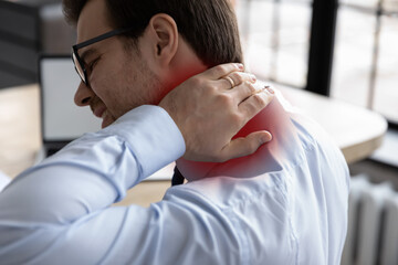 Rear view unhealthy millennial male manager worker touching inflamed place, suffering from strong neck pain, chronic ache muscular tension or nerve entrapment, sedentary office lifestyle concept.