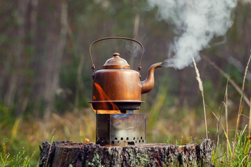 Vintage copper kettle on a tourist stove on an old stump in the forest. The background of the trees...