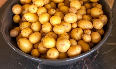 Washed small potatoes in a metal bowl on the background of the table in the kitchen