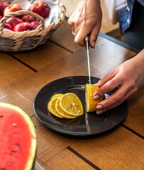 The process of slicing a lemon with a knife in the hands of a person close-up on the background of the table in the kitchen