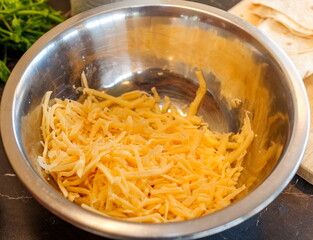 Grated hard cheese in a metal bowl close - up on the background of the table in the kitchen