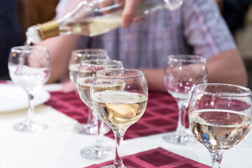 Waiter's hand pours white wine into glasses in a restaurant
