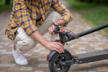 Man sitting on his hunkers and fixing his scooter