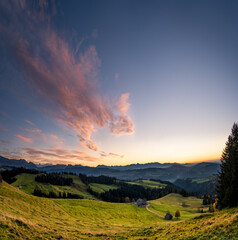 Fototapeta na wymiar overview swiss landscape with hills forests mountains in warm color during sunset or sunrise and epic sky