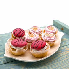 On a blue wooden tray, on a white porcelain plate, a set of biscuit cakes. Decorated with whipped cream, raspberry meringues, chopped nuts, chocolate glaze. White background.