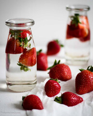 Strawberries in water in glass bottles on a light background