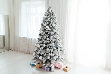 white snow Christmas tree with gifts at the window of the new year interior