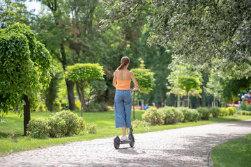 Girl in orange top riding a scooter in the park