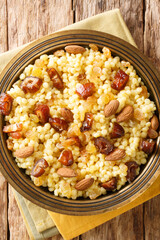 Mesfouf is a steamed Couscous with olive oil, butter, nuts and raisins close-up in a plate on the table. vertical top view from above