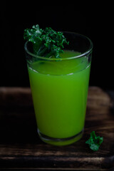 Green drink in a glass with kale on a wooden dark background.