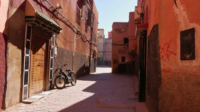 Black colored old motor bike leaning at the wall in a narrow empty alley in the historic center (Medina) of Marrakesh, Morocco on a sunny day.