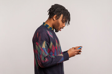 Extremely surprised african man with dreadlocks widely open his mouth holding mobile phone, wondered shocked with bonuses. Indoor studio shot isolated on gray background