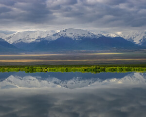 View of the snow-capped Trans-Alai mountain range in southern Kyrgyzstan with reflection in Kyzyl Suu river in the foreground