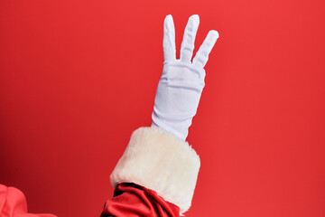 Hand of a man wearing santa claus costume and gloves over red background counting number 3 showing three fingers