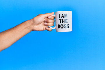 Hand of hispanic man holding i am the boss coffee cup over isolated blue background.