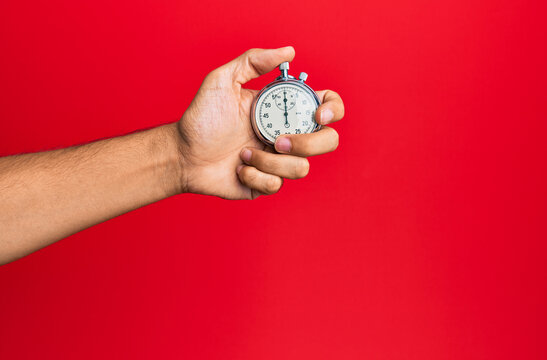 Hand of young hispanic man using stopwatch over isolated red background.