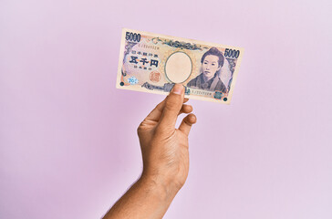 Hispanic hand holding one 5000 japanese yen banknote over isolated pink background.