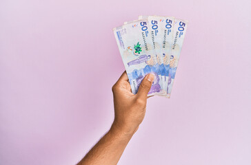 Hispanic hand holding 50 colombian pesos  banknotes over isolated pink background.